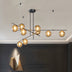 Modern chandelier with black metal frame and amber glass globe shades illuminated against a cream ceiling above dark paneled walls.