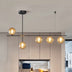 # Modern black linear chandelier with five amber glass globe pendants illuminating a contemporary kitchen.
