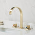 Brushed gold three-piece bathroom faucet with curved spout on white marble countertop.