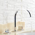 Chrome and black arc bathroom faucet with dual handles displayed on white sink against brick tile backdrop.