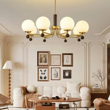 "Ralie chandelier with iron, wood, and glass globes hanging in a living room with a white sofa, framed art, and a floor lamp."