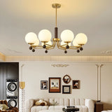 "Ralie chandelier with iron, wood, and glass globes hanging in a living room with a white sofa and framed pictures."