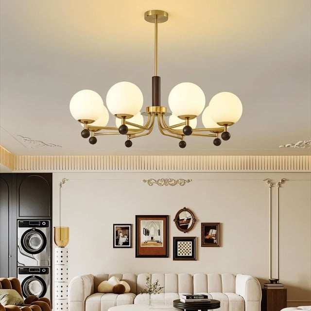 "Ralie chandelier with iron, wood, and glass globes hanging in a living room with a white sofa and framed pictures."