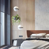 "Modern pendant lights with spherical frosted glass diffusers and iron bands, combined with hanging planters in a contemporary bedroom."