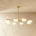 Gold branch chandelier with six frosted white globe lights against gray textured wall in modern interior setting.