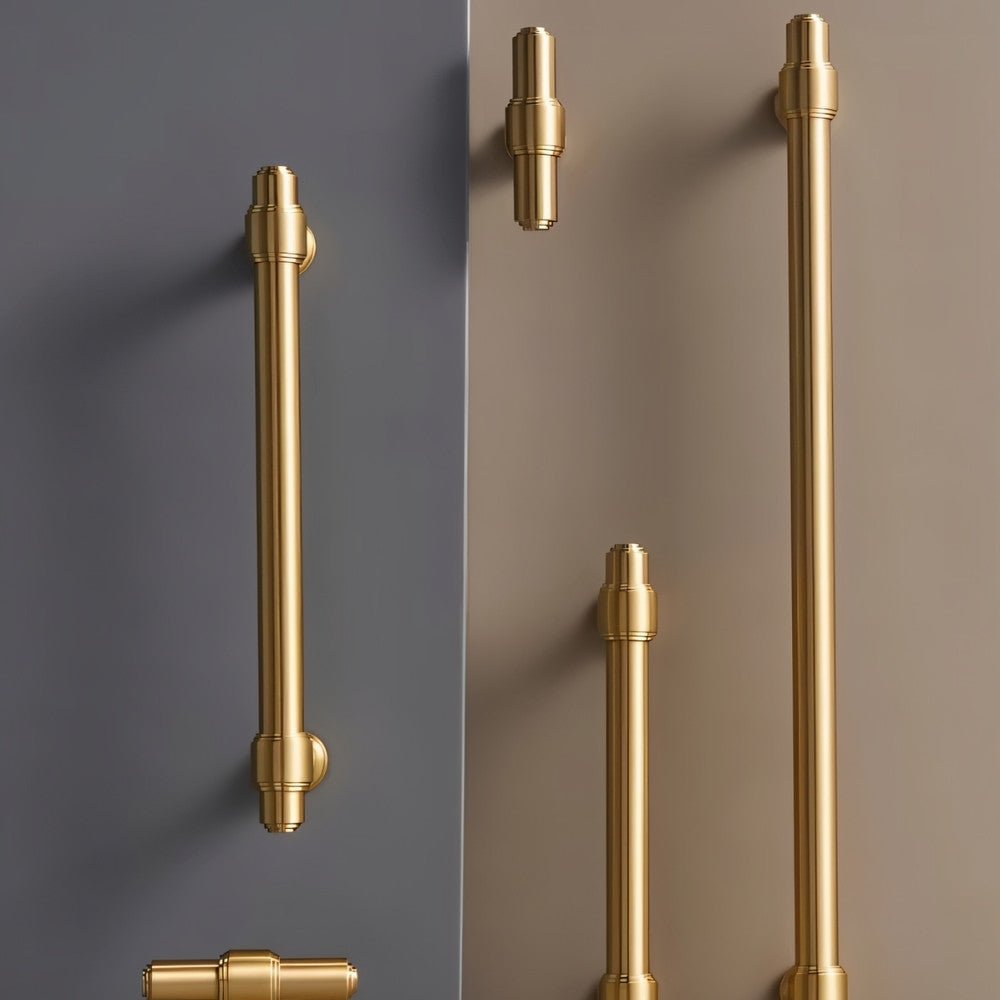 "A set of solid brass knobs and pull bars with a cylindrical design and machined details, arranged on a two-tone background."