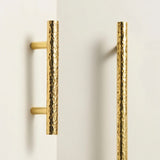 "Pair of hammered brass pull bars with a textured, artisanal finish mounted on a white cabinet."