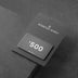 Black gift card displaying "$500" on textured dark surface with packaging.
