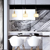 "Three modern pendant lights with rounded alabaster shades and brass accents hanging above a kitchen island with a marble countertop."
