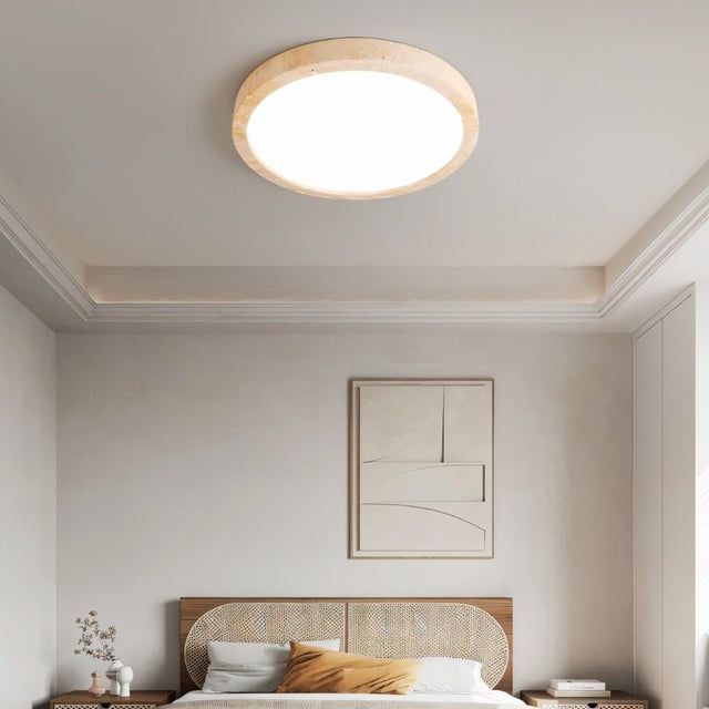 "A minimalist, natural travertine ceiling light illuminates a modern bedroom with artwork and soft, uniform light."