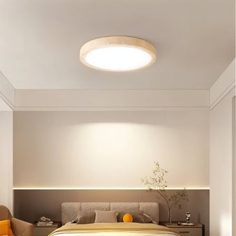 "A minimalist, natural travertine Richna ceiling light illuminates a modern bedroom with soft, uniform light."