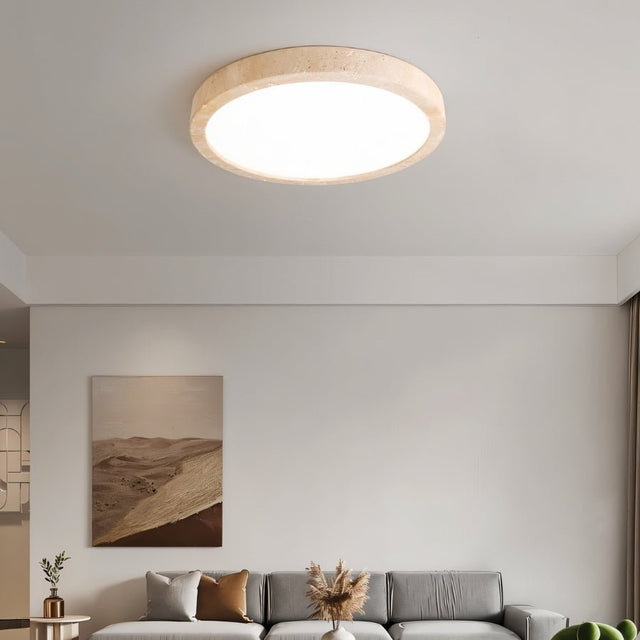 "A minimalist, natural travertine ceiling light illuminates a modern living room with artwork and soft, uniform light."