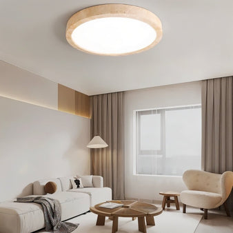 "A minimalist, natural travertine Richna ceiling light illuminates a modern living room with soft, uniform light."