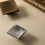 "Close-up studio shot of ridged square brass cabinet knobs in silver and bronze finishes on a neutral background."