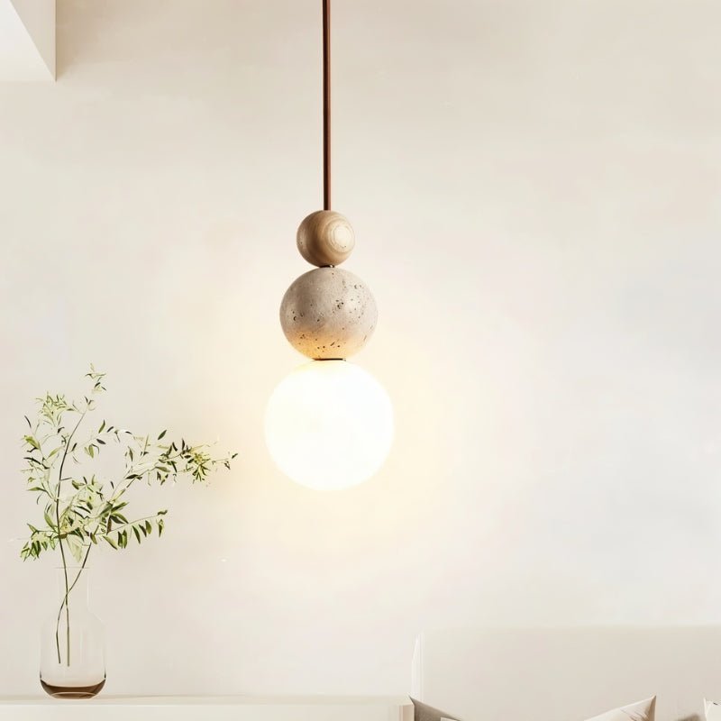 "Single sculptural pendant light with stacked travertine, wood, and metal elements, featuring a frosted glass diffuser."