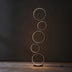 Five stacked neon rings in warm white glow arranged vertically on a dark gallery floor and wall.