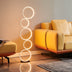 Vertical stacked neon ring floor lamp with warm white glow beside yellow leather sectional sofa in modern living room.