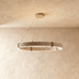 Circular concrete pendant light with warm brass accents, suspended in studio setting above potted flowers.