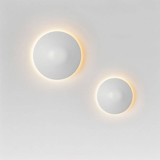Two Rochi Wall Lamps in white aluminum mounted on a wall, emitting warm ambient light in a minimalist arrangement.
