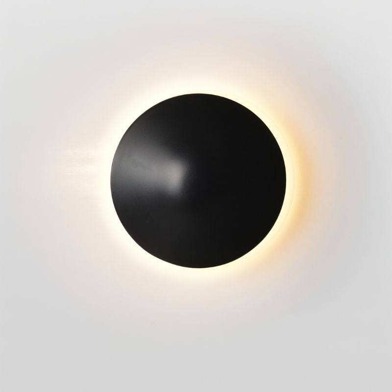 Close-up of the Rochi Wall Lamp in black aluminum, showcasing its sleek, asymmetrical design and warm backlit glow.