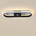 Modern oval LED ceiling light with black and white finish and motion sensor, mounted on beige wall.