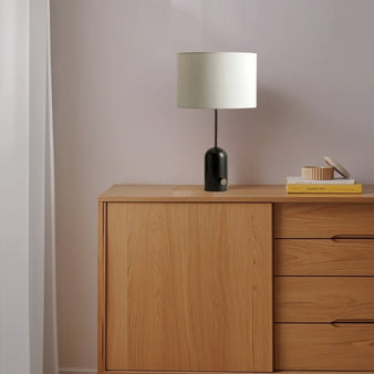 "Table lamp with black marble base and drum lampshade on a wooden dresser, minimalist bedroom decor, soft lighting ambiance"