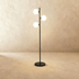 Three-globe black floor lamp with white frosted glass shades next to gray upholstered chair in modern interior setting.