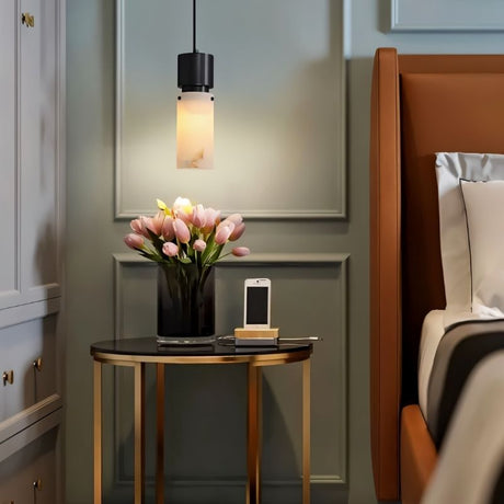 "Modern pendant light with a cylindrical alabaster shade and a black frame, illuminating a bedside table in a contemporary bedroom."