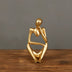 Gold-finished abstract figurine in a contemplative seated pose on a wooden surface.