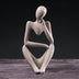 Stone figurine of a seated woman in contemplative pose against a black background.