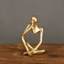 Gold-finished abstract figurine of a seated contemplative figure displayed on a wooden surface.