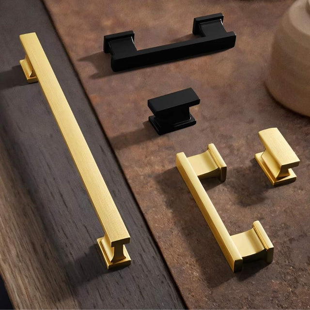 "Set of gold and black zinc alloy knobs and pull bars with angular design, displayed on a wooden surface."