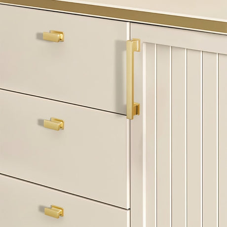 "Gold zinc alloy knobs and pull bar with angular design on cream-colored cabinets."