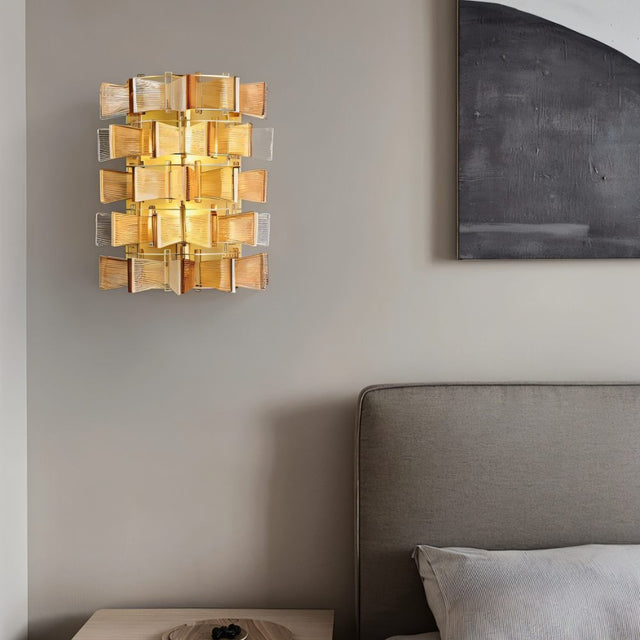 "Iron Salane wall lamp with layered amber glass panels, mounted on a grey wall above a bedside table with an artwork."