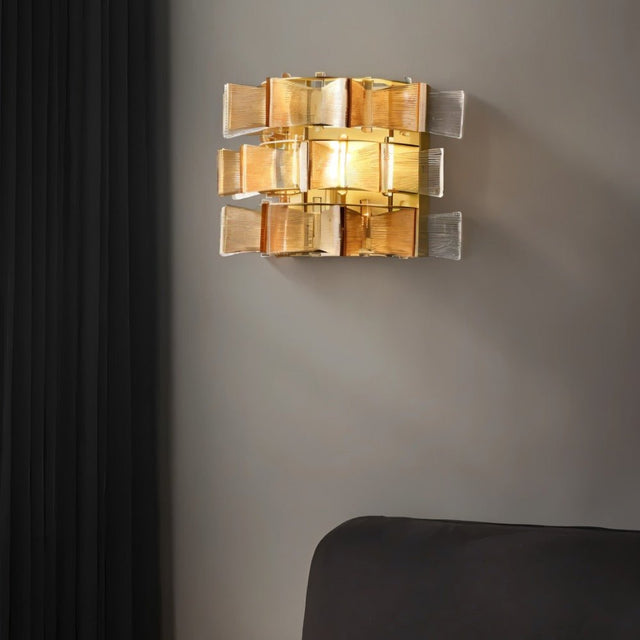 "Iron Salane wall lamp with layered amber glass panels, mounted on a grey wall beside a dark curtain."