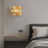"Iron Salane wall lamp with layered amber glass panels, mounted on a grey wall above a bedside table."