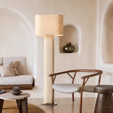 "Modern floor lamp with a cylindrical iron base and a fabric shade in a living room with an arched wall niche, a chair, and a sofa."