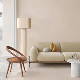 "Modern floor lamp with a cylindrical iron base and a fabric shade in a minimalist living room with a wooden chair and a sofa."