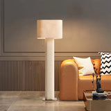 "Modern floor lamp with a cylindrical iron base and a fabric shade illuminating a living room with a sofa and decorative items."