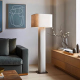 "Modern floor lamp with a cylindrical iron base and a fabric shade in a contemporary living room setting with a sofa and artwork."