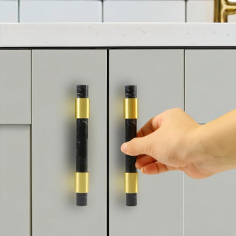 "A hand opening a cabinet with luxurious black marble handles accented with polished brass, in a contemporary interior."