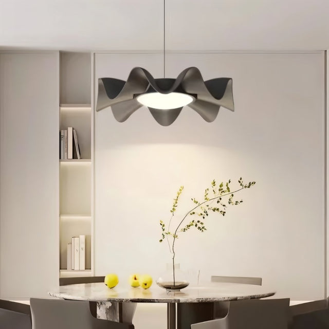 "Sculptural pendant light with a wave-like iron frame and acrylic diffuser hangs above a modern dining table, adding a touch of artistic elegance."