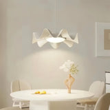 "White sculptural pendant light with a wave-like iron frame and acrylic diffuser hangs above a modern dining table, providing a soft and elegant illumination."