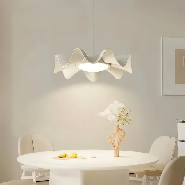 "White sculptural pendant light with a wave-like iron frame and acrylic diffuser hangs above a modern dining table, providing a soft and elegant illumination."