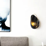 "Modern black resin wall lamp with gold sphere and metal hoop, displayed beside an abstract artwork."