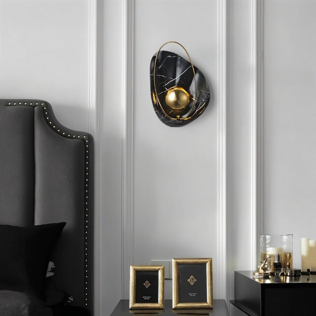 "Modern black resin wall lamp with gold sphere and metal hoop, mounted in a bedroom."