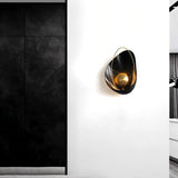 "Modern black resin wall lamp with gold sphere and metal hoop, mounted on a white wall in a contemporary setting."