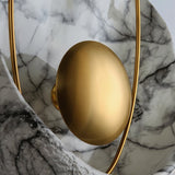 "Close-up of a modern wall lamp with gold sphere, metal hoop, and resin shell with marble veining."