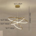 Modern brass LED chandelier with three curved rings suspended from ceiling in neutral interior space.