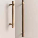 "Two antique brass pull bars with cylindrical design and subtle accents, mounted vertically on white cabinet doors."